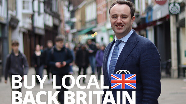 Meon Valley Times Danny Chambers MP standing on Winchester High Street, wearing a navy blazer, navy and white polka dot tie, and a pale blue shirt.